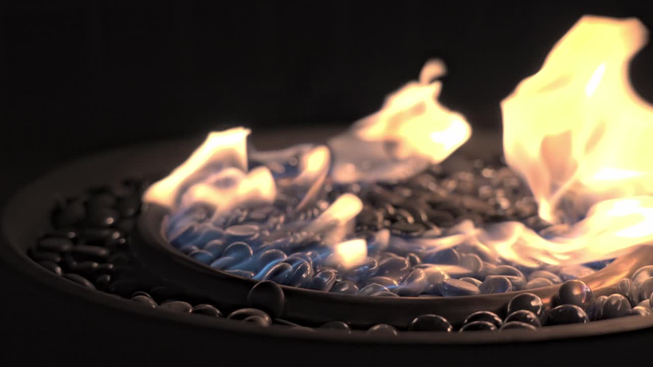 Close-up view of a modern gas-powered fire pit featuring decorative glass marbles. The flames flicker and dance above the shimmering surface