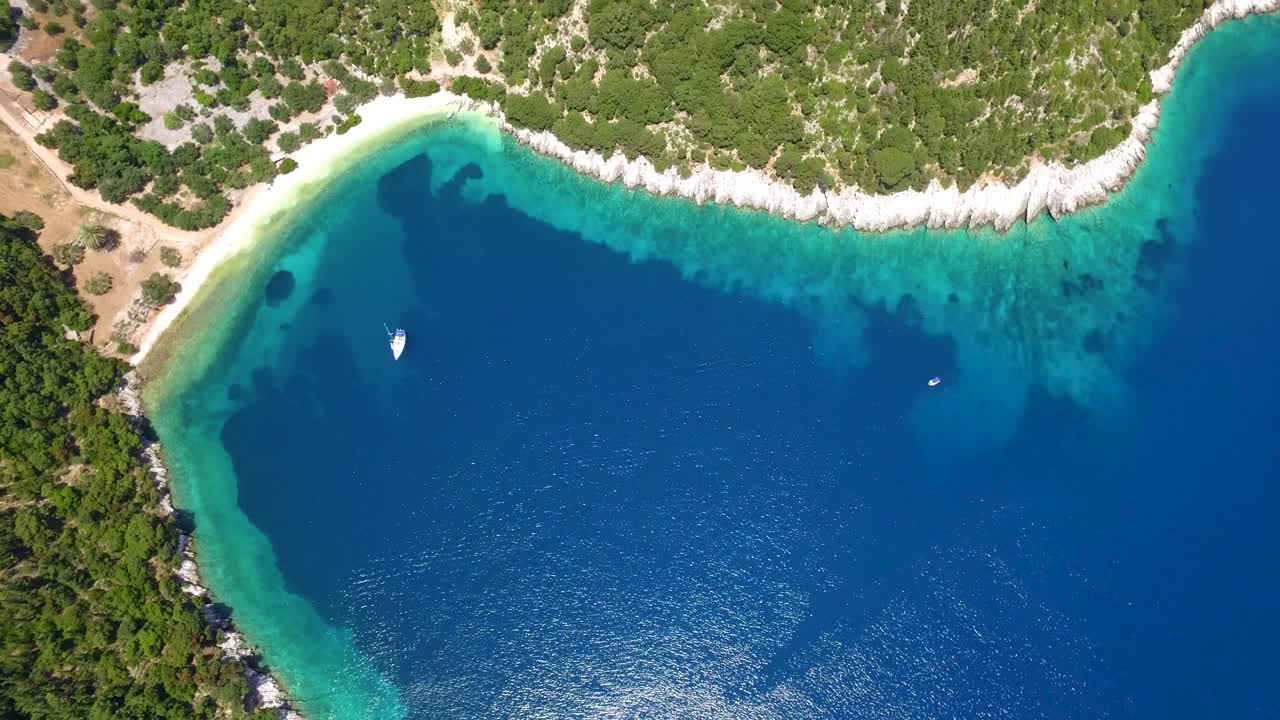 Acque cristalline lambiscono una cala verde lussureggiante sull'isola di Cefalonia, vista aerea, giornata di sole.
