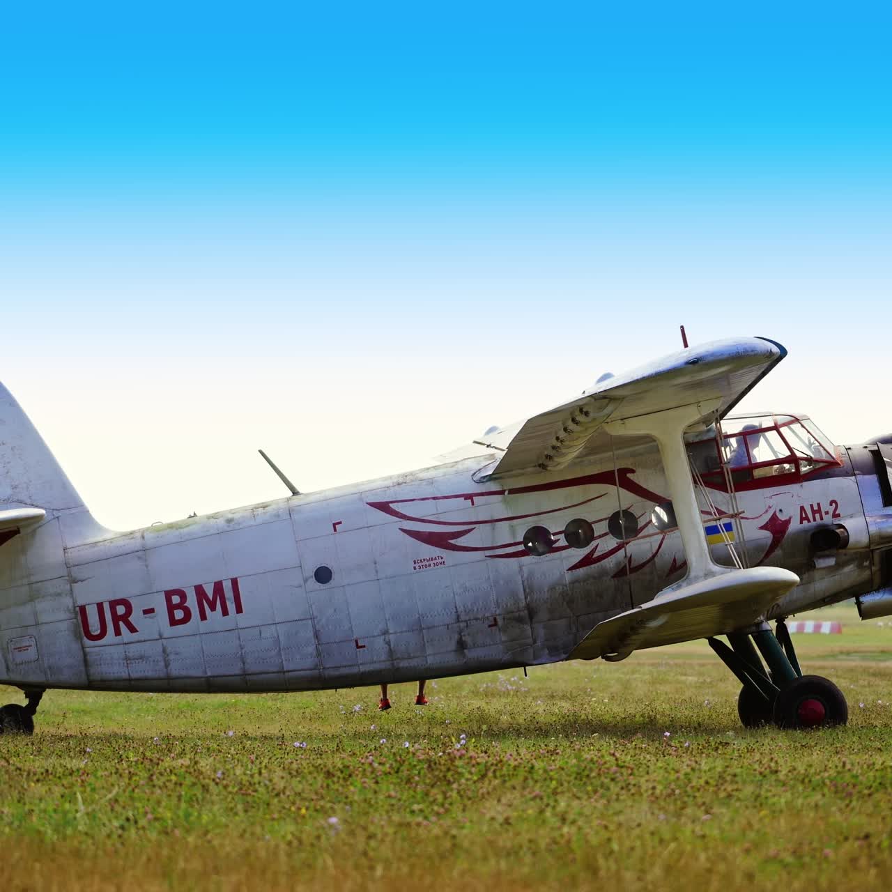 Few little airplanes standing in the row outdoors. One of the aircrafts starts the engine and moves forward