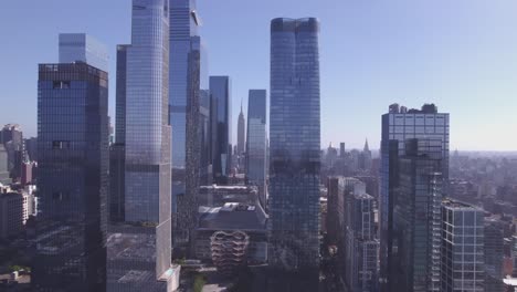 drone push-in toward the vessel in hudson yards, framed by tall modern skyscrapers under a clear blue sky in manhattan, new york city