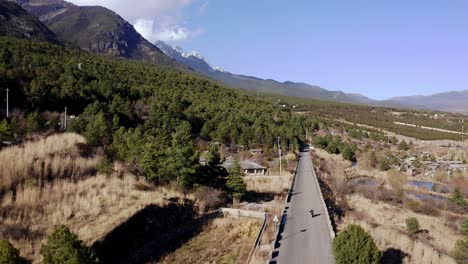 People-riding-scooter-motorcycle-on-remote-mountain-road,-Yulong-China,-aerial