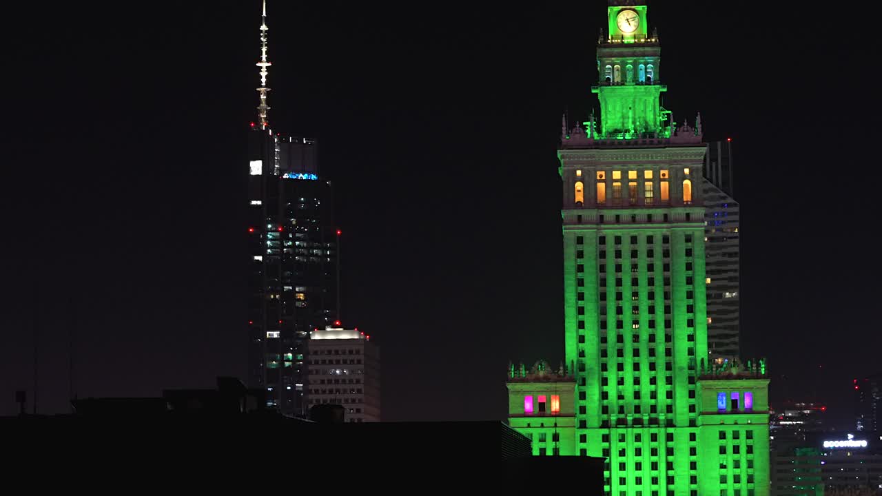 Inquadratura aerea che rivela l'iconico Palazzo della Cultura e della Scienza illuminato di un verde vibrante contro il cielo notturno a Varsavia, periodo natalizio