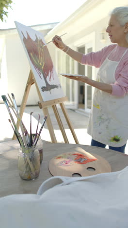 vertical video of happy senior biracial woman painting at balcony, slow motion