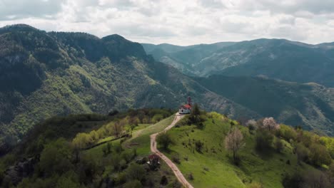 Aerial-view-of-small-church-at-the-top-of-the-hill-surrounded-by-green-mountains