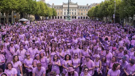 a vibrant gathering of enthusiastic individuals dressed in pink attire celebrating together in a bustling urban square surrounded by greenery and historic buildings