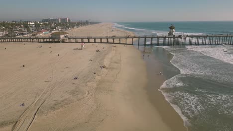 Experimente-La-Belleza-Del-Paseo-Marítimo-Del-Muelle-De-Huntington-Pacific-Con-Este-Cautivador-Lapso-De-Tiempo-De-Drones,-Que-Muestra-Las-Olas-Y-La-Vida-Costera-De-Un-Día-Soleado