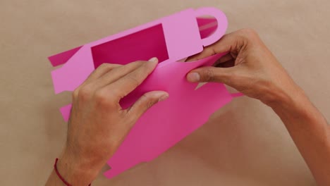 hands assembling bright pink confectionery box on beige surface