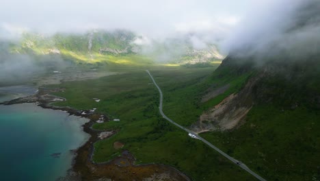 an aerial view reveals cars driving through while low-hanging clouds are above, in the captivating landscape of the lofoten islands, norway