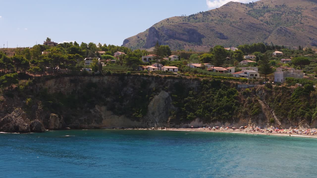 Panning left aerial drone shot of coastal cliff by a Mediterranean beach in Sicily, Italy, capturing summer tourism and scenic landscape