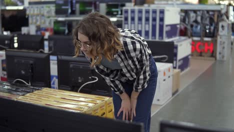 smart modern female customer choosing large tv-sets at electronics store. new screen generations. look closely on large thin tv in the store