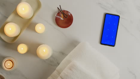 Overhead-View-Looking-Down-On-Still-Life-Of-Blue-Screen-Mobile-Phone-With-Lit-Candles-And-Incense-Stick-As-Part-Of-Relaxing-Spa-Day-Decor