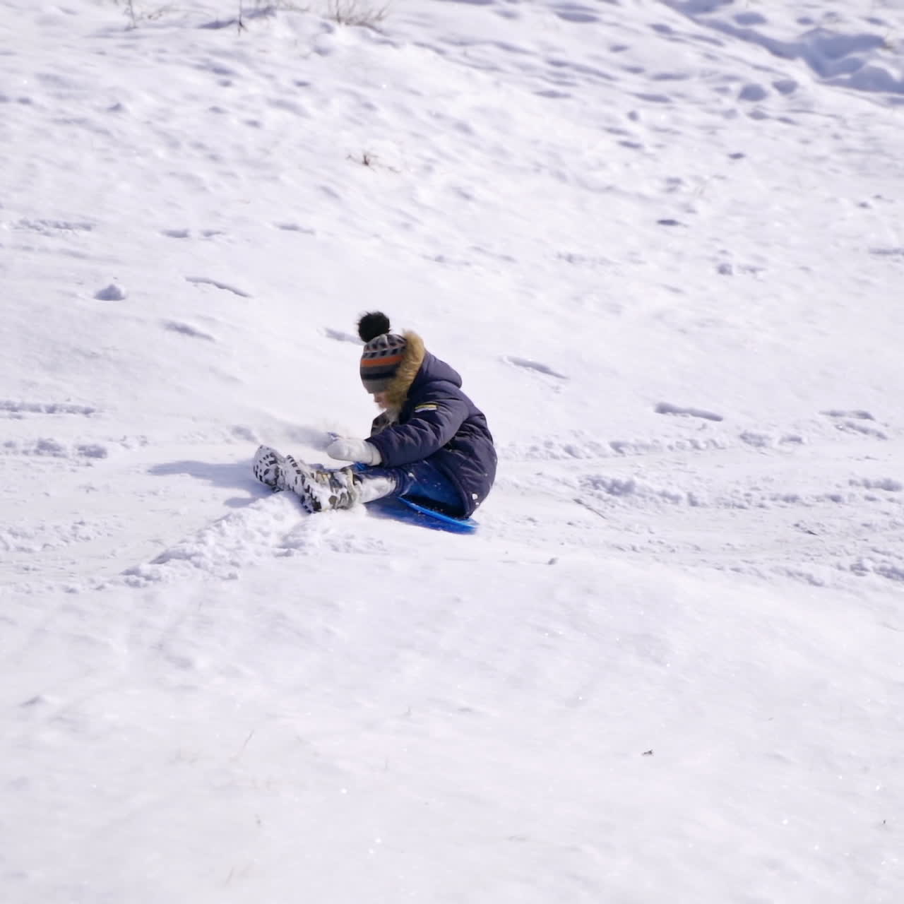 Little boy sledging in winter. Happy child riding down from a snowy slide outdoors. Winter games and fun. Slow motion.