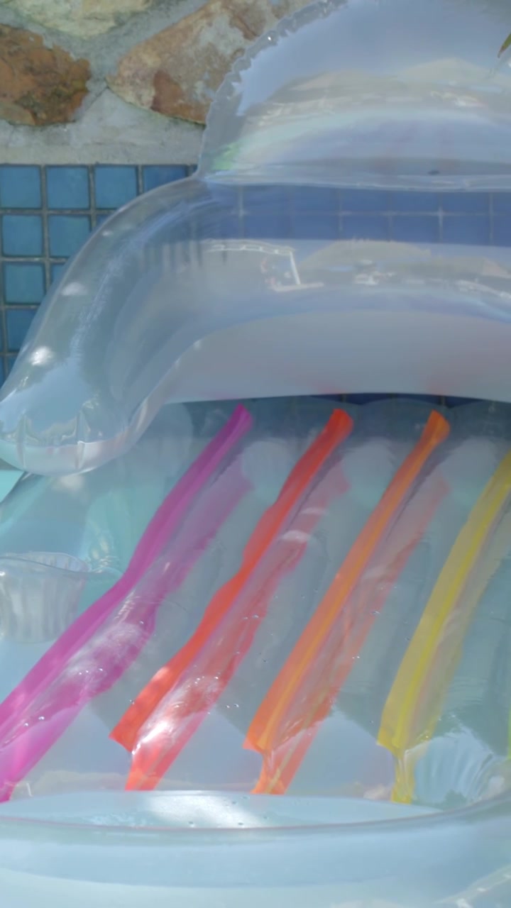 Vertical video: Bobbing inflatable lounger catching sun by pool edge, showing six colored tubes