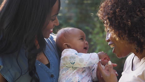 grandmother with adult daughter and baby granddaughter playing in garden at home together