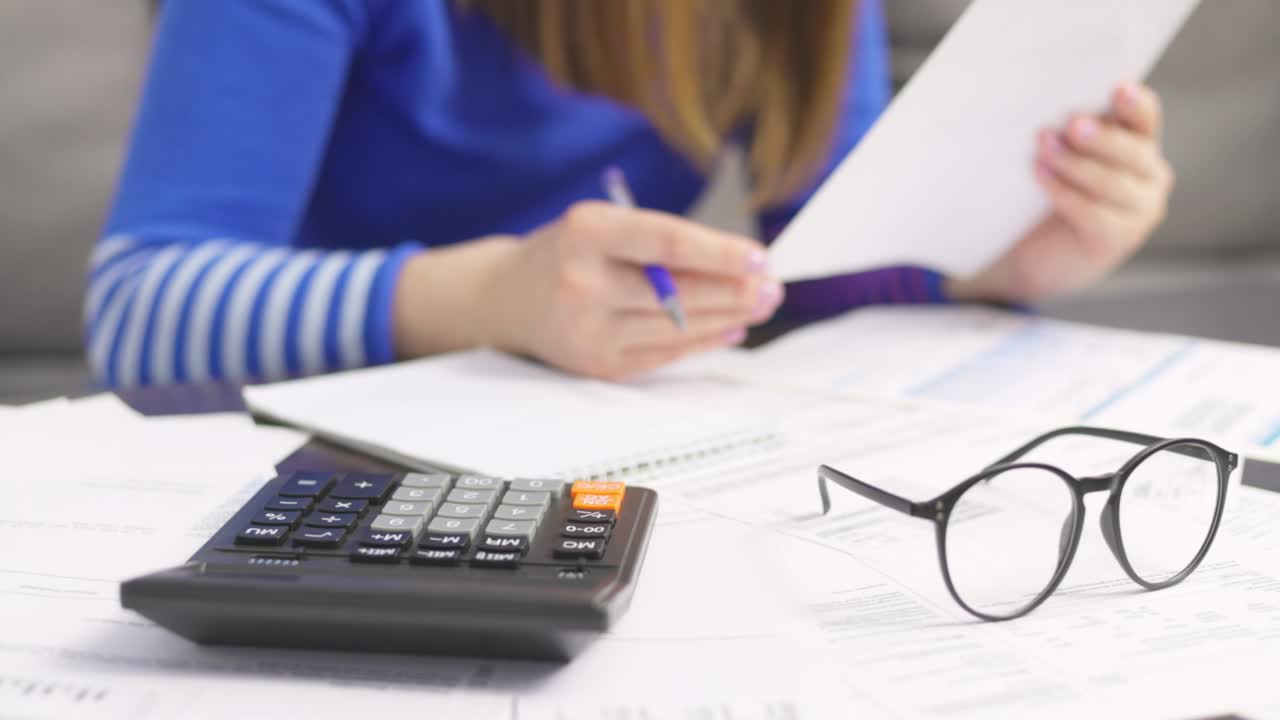 mujer usando calculadora para calcular facturas domésticas en el hogar, haciendo papeleo para pagar impuestos