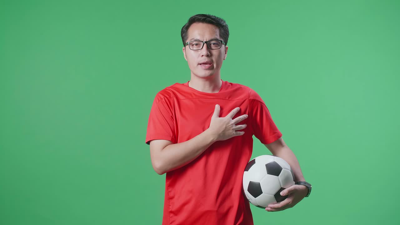 hombre asiático con una pelota cantando el himno nacional mientras anima al fútbol en el fondo de la pantalla verde