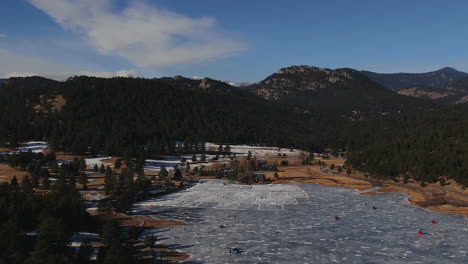 drones cinematográficos aéreos casa de lago de hoja perenne con pistas de hielo y personas patinando o jugando al hockey en colorado con movimiento hacia abajo