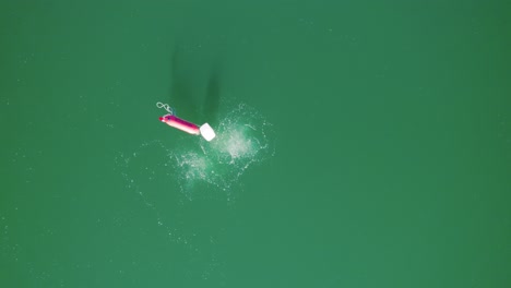 Vista-Aérea-De-Una-Boya-Roja-En-Un-Lago,-Los-Buceadores-Suben-A-La-Superficie