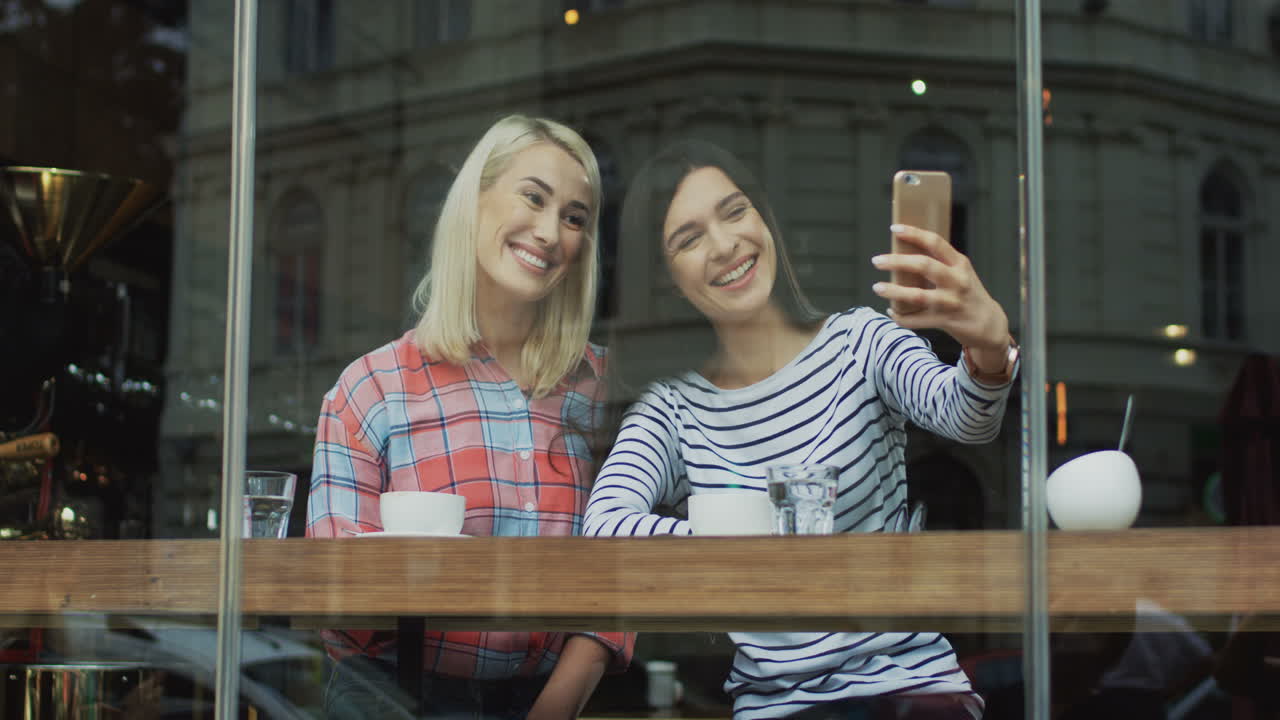 dos hermosas mujeres posando y tomando fotos selfie mientras están sentadas en un café