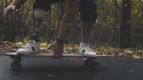 a young man with a metal bionic prosthetic leg is riding a skateboard in the autumn forest. an artificial leg pushes off the asphalt on a skateboard