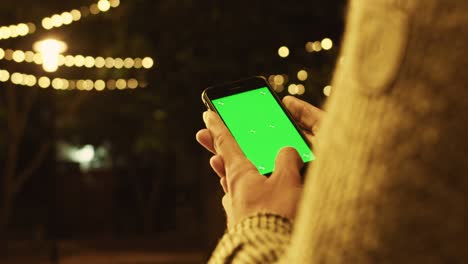 man hands holding use smartphone with vertical green screen on night city colorful. communication device hands digital gadget phone touchscreen mobile