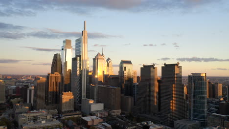 aerial drone fly away view of the downtown philadelphia skyline featuring tall, glass skyscrapers at sunset with gold and purple light showing the comcast technology center