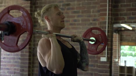 tattoo man muscles in home gym doing barbell shoulder press