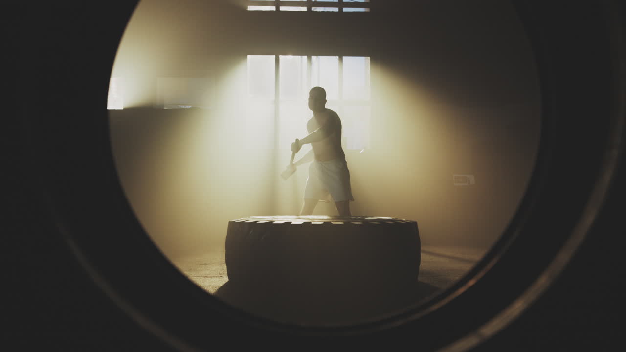 Man working out with a sledgehammer on a tire in a gym