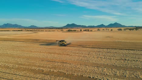 Vista-Aérea-Sobre-El-Campo-De-Trigo-Y-Una-Cosechadora-Con-El-Parque-Nacional-Stirling-Range-Al-Fondo,-Australia-Occidental