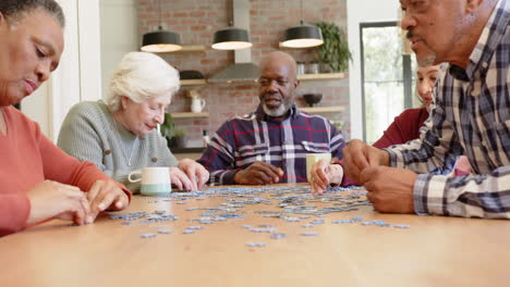 happy diverse senior female and male friends talking and doing jigsaw puzzle in kitchen, slow motion