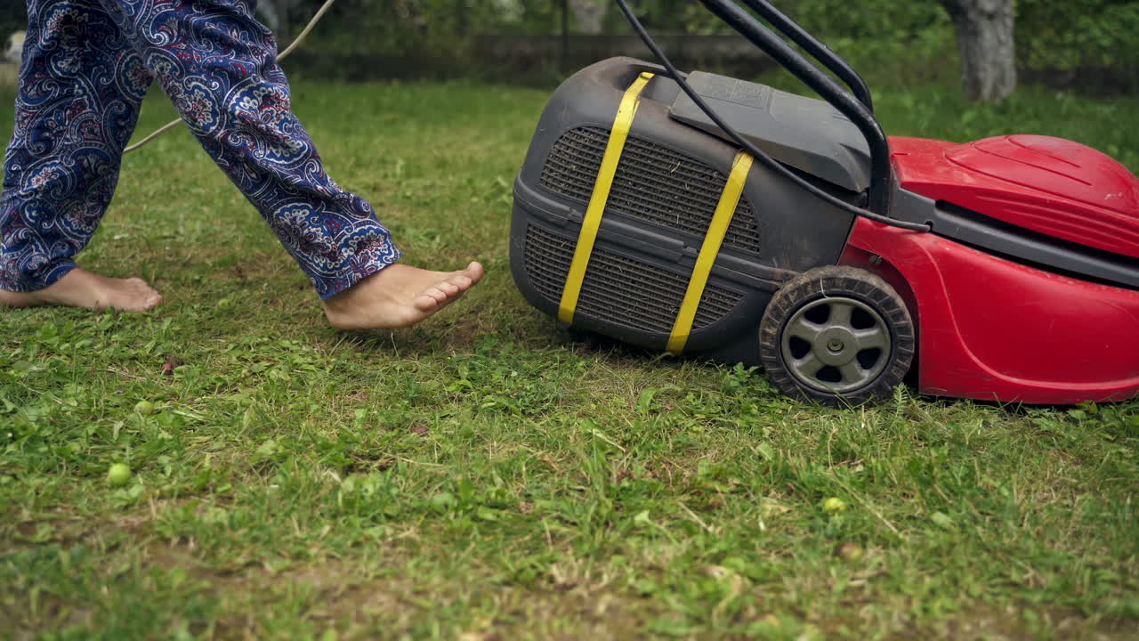 Corded lawn-mower works in the garden. Woman cutting green grass with mowing machine in the backyard. Gardening in summer.