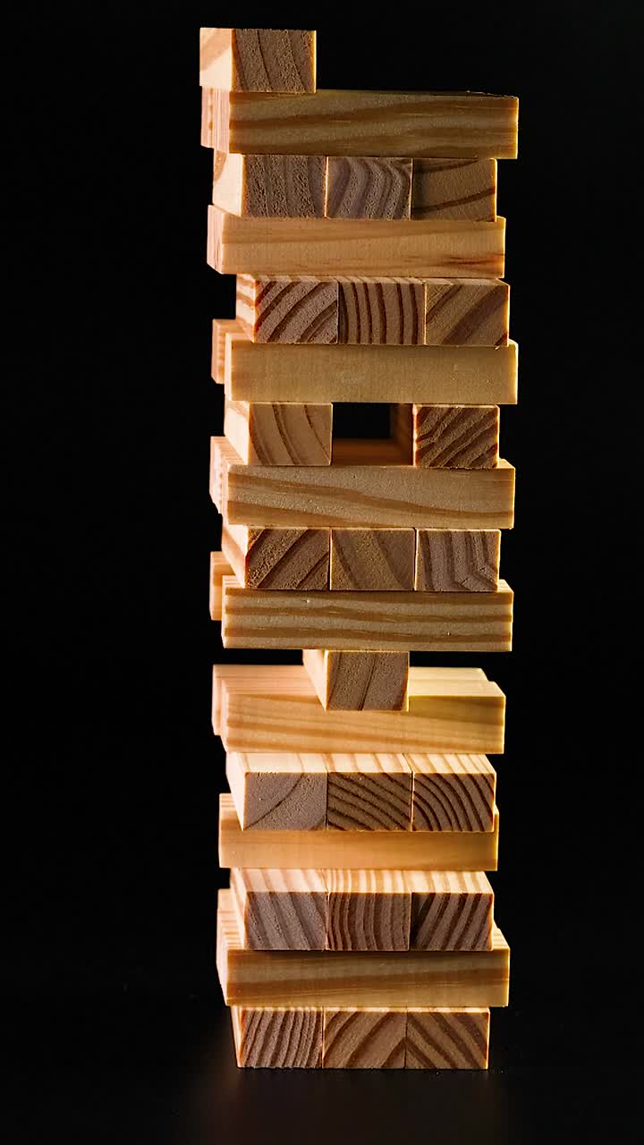 Una mano rimuove con attenzione e riposiziona un blocco di legno su una torre alta su sfondo nero
