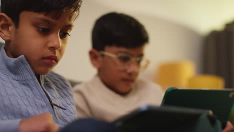 two young boys sitting on sofa at home playing games or streaming onto digital tablets 18