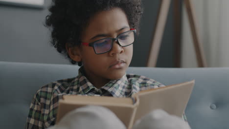 young boy reading a book on a sofa