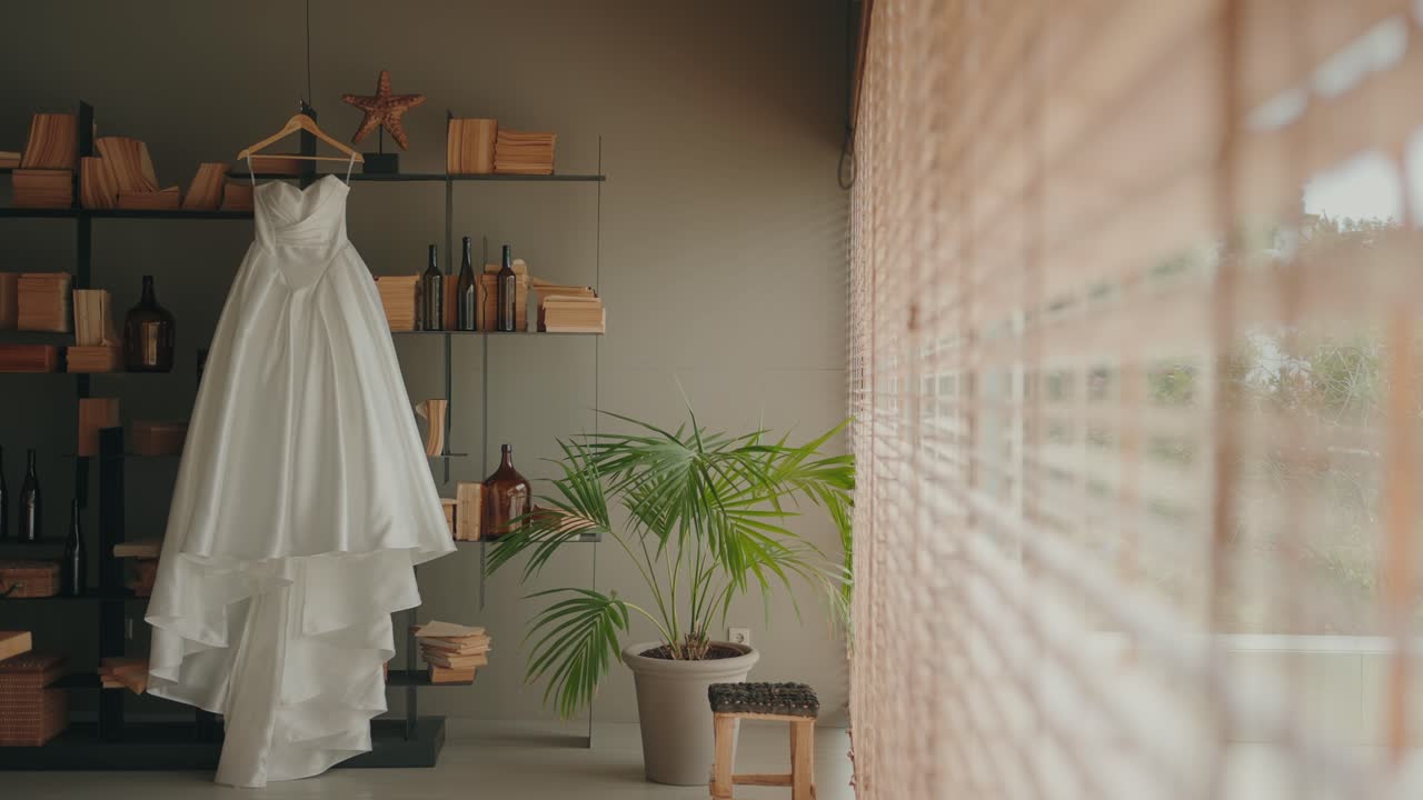 Wide shot of elegant wedding gown displayed near window with decor