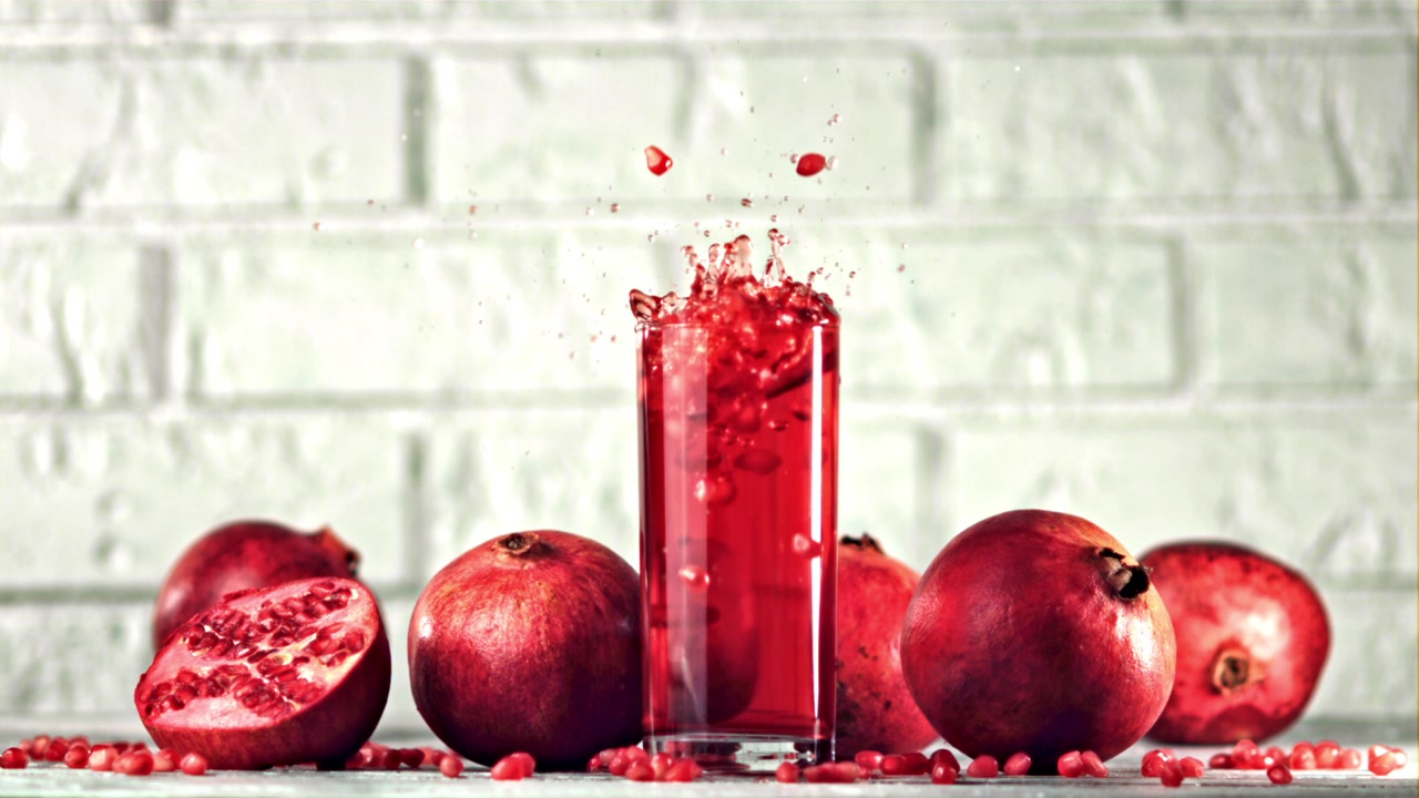 Slowmotion granatæblekerner, der sprøjter ned i et glas rød juice