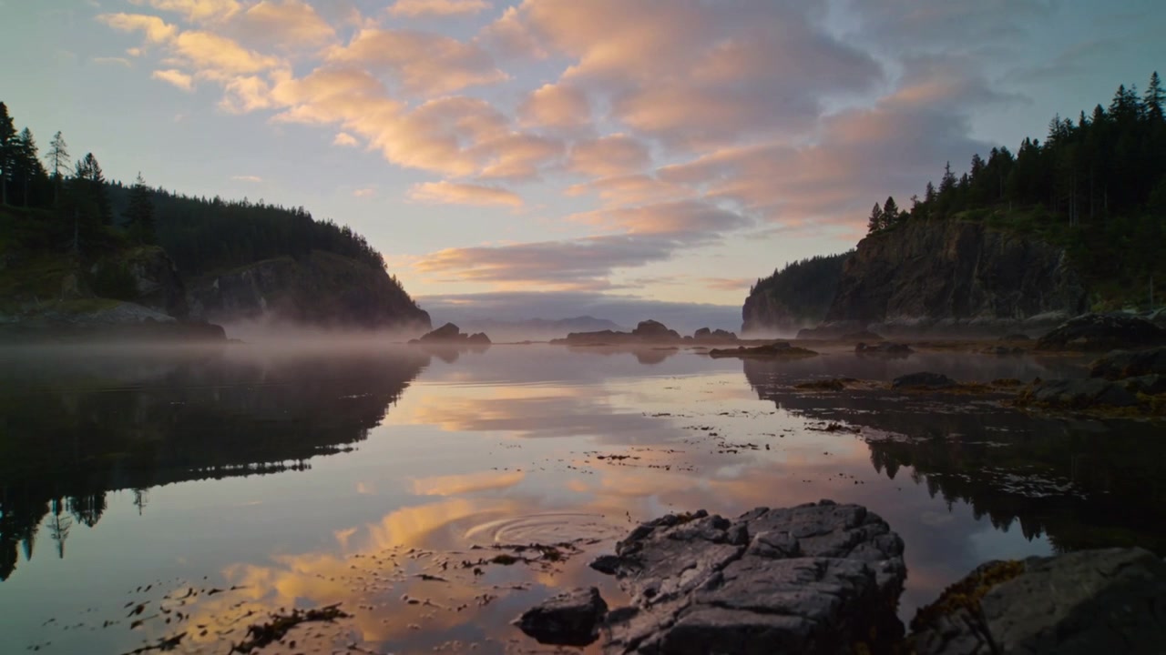 Camera panning revealing center calm water reflecting pink clouds at rocky inlet, exposing rocks