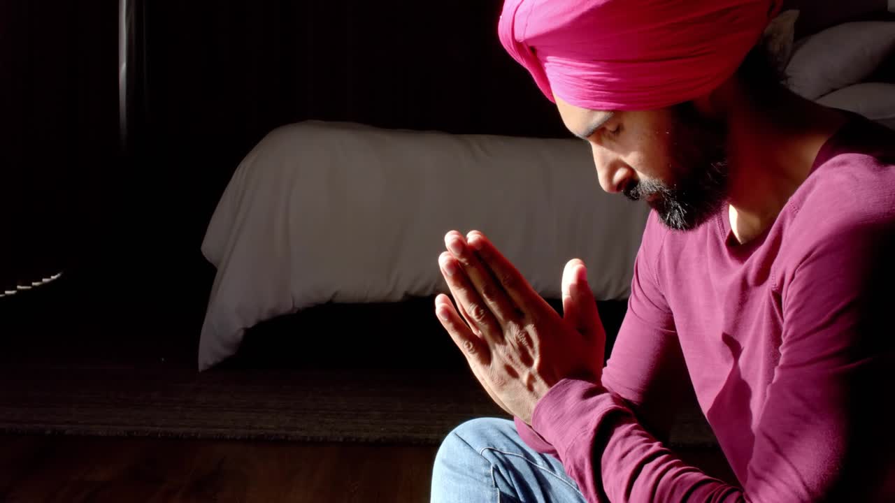 Man sitting by bed, holding hands, bowing while moving bokeh overlays revealing turban for wellness