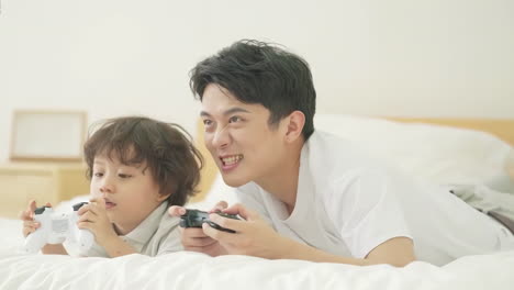 Happy-family-father,-child-son-playing-games-and-videos-on-bed-at-home-joyful-atmosphere-enjoying-leisure-time-in-living-room