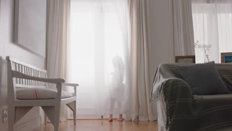 happy little girl running through house wearing tutu opening curtains looking out window at beautiful new day with bright sunlight playful child feeling positive 4k footage