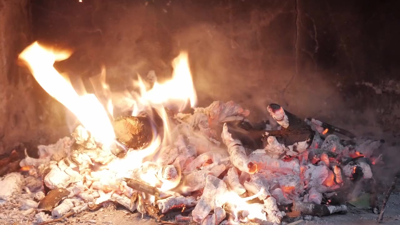 Bir şöminede kızgın korları ve külleri karıştıran el, yemek pişirmek için parlayan közleri yayıyor.