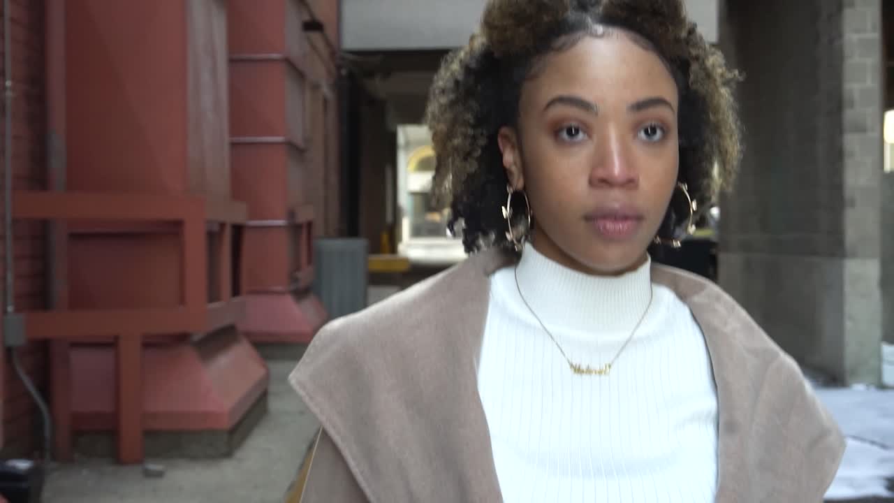 modelo negro camina por un callejón cerca de una pared de ladrillos