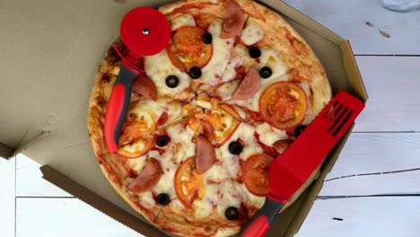 fresh round pizza with tomatoes, sausage, mozzarella and olives in cardboard box rotates slowly.