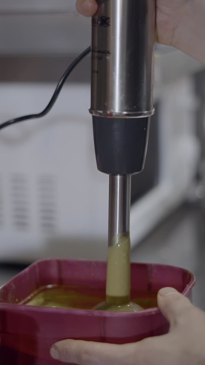Blending a green liquid with a hand blender in a kitchen