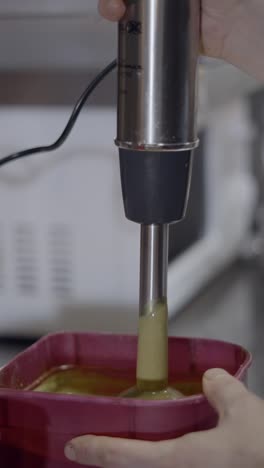 blending a green liquid with a hand blender in a kitchen