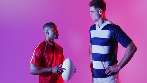 Diverse-male-rugby-players-with-rugby-ball-over-pink-lighting
