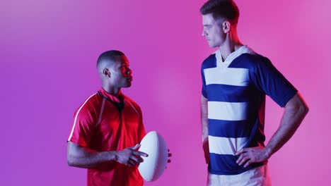 diverse male rugby players with rugby ball over pink lighting