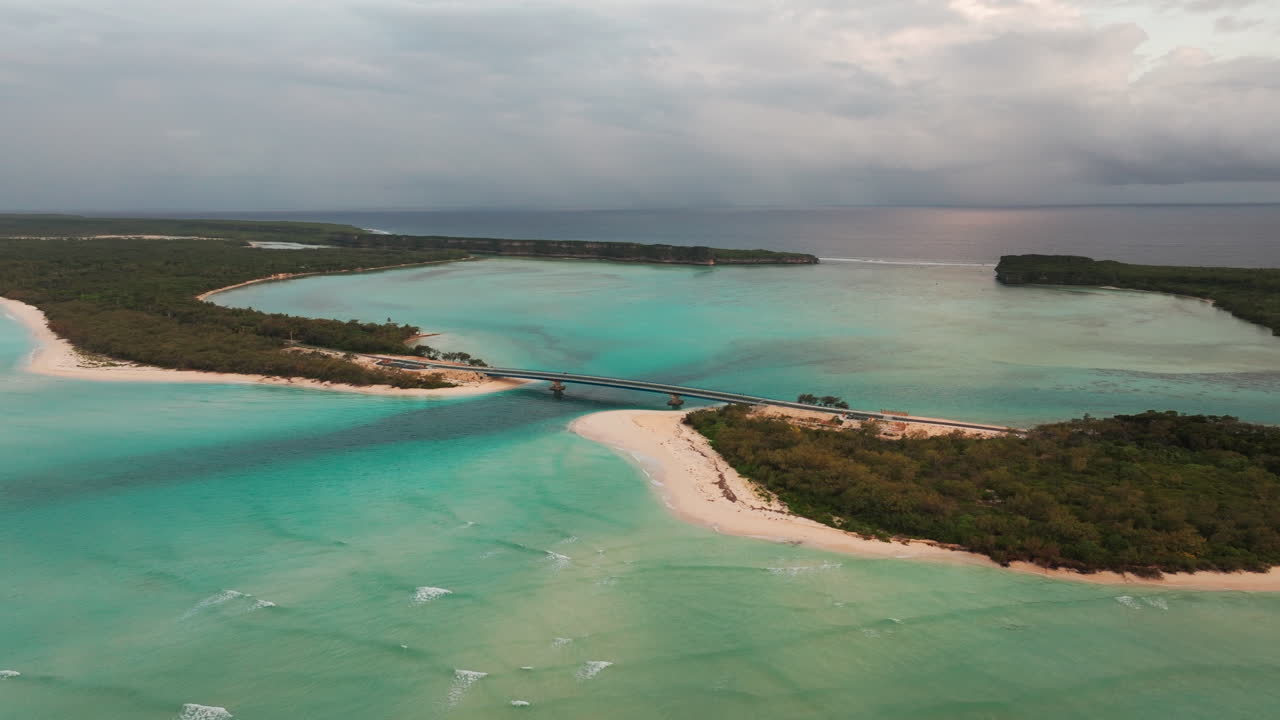 Wide drone view of Mouly Bridge surrounded by turquoise lagoon waters, sandy beaches, and green vegetation in Lekini Bay, Ouvea, New Caledonia
