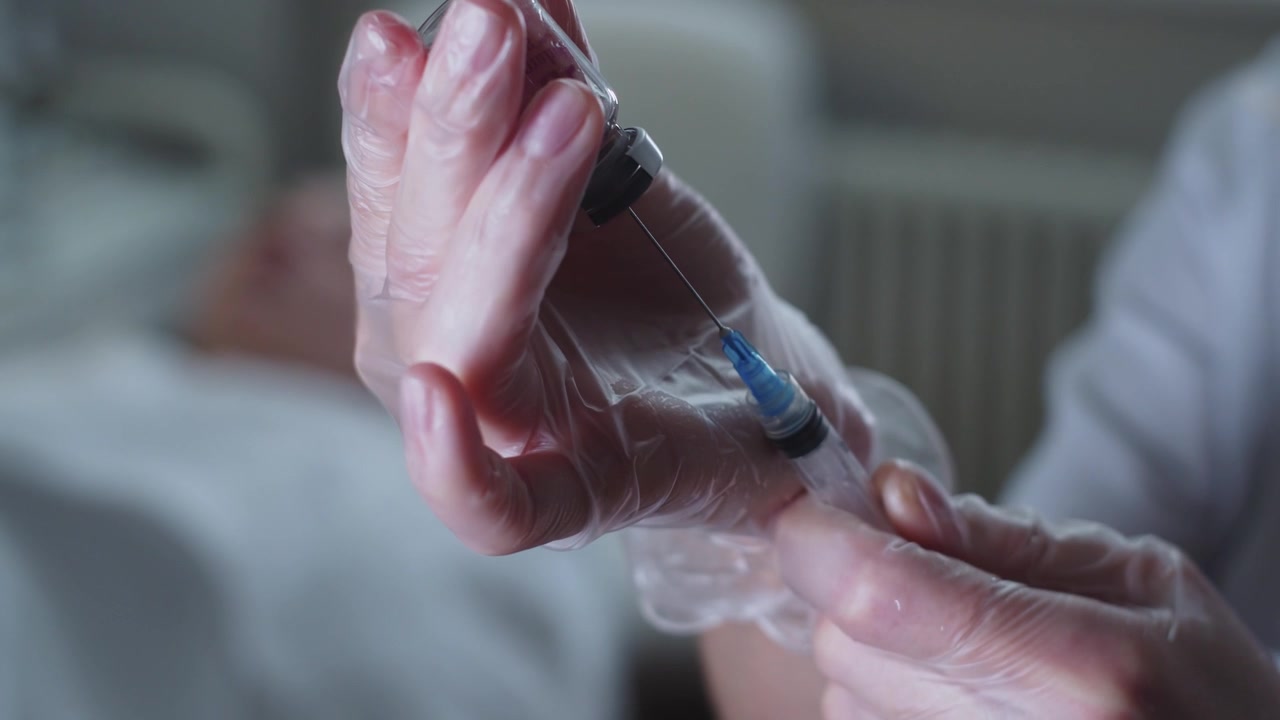 A health worker draws a solution from a bottle into a syringe