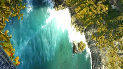 Vertical-slow-motion-tilt-up-shot-of-the-beautiful-cliffs-in-Bali-at-Pura-Uluwatu-temple-in-Bali-with-view-of-the-rocks-and-the-blue-sea-with-high-waves-during-a-sunny-summer-day